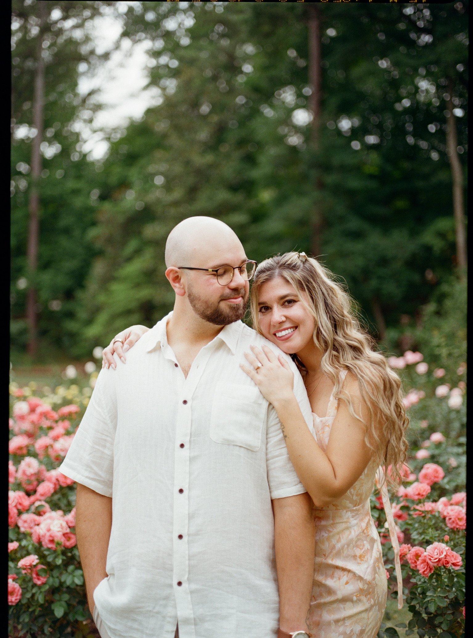 Nicole resting her head on Ian’s shoulder in front of the pink roses, his eyes on her.