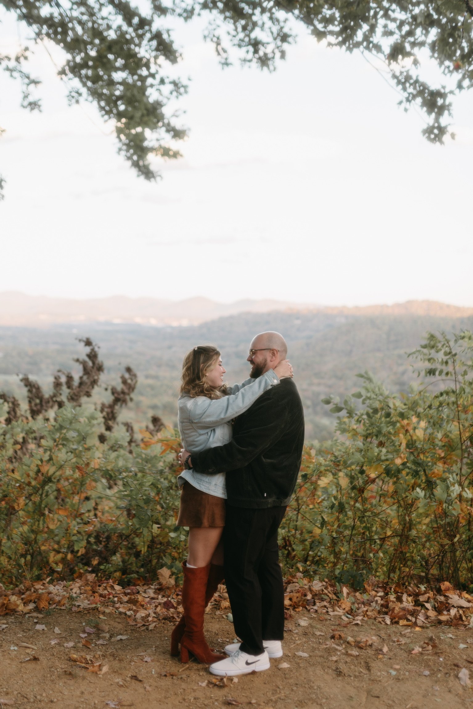Nicole and Ian embracing at the overlook edge, the valley in soft evening light behind them.