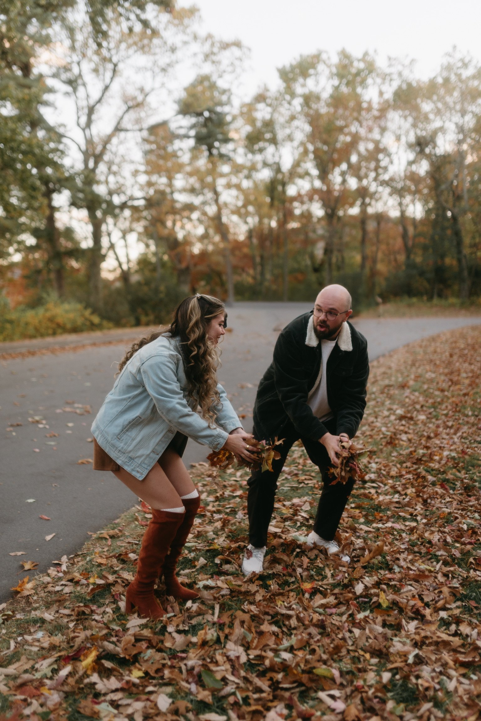 Nicole and Ian scooping up armfuls of fallen leaves at the roadside.