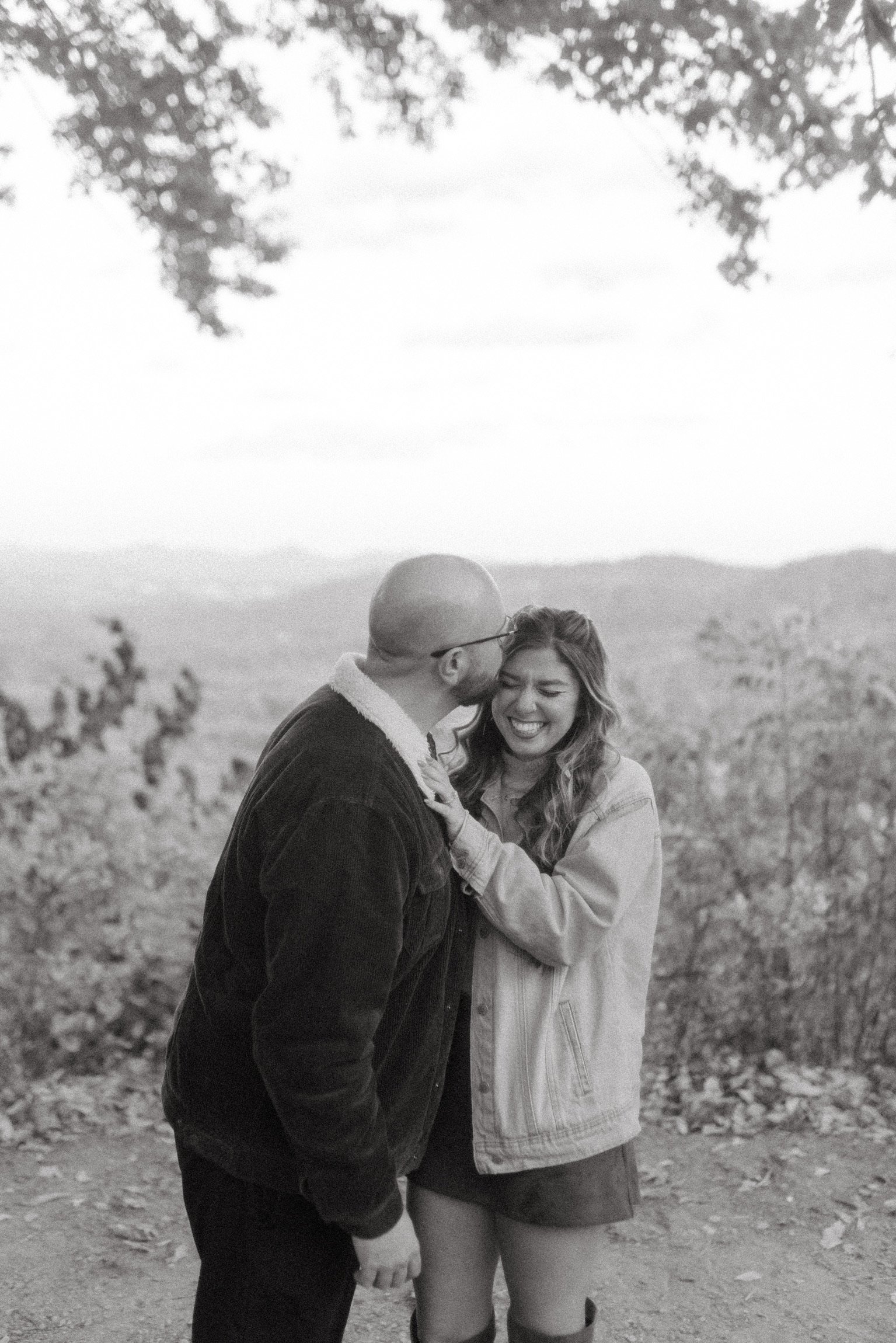 In black and white: Ian kissing the side of Nicole’s head as she laughs, the mountains behind.