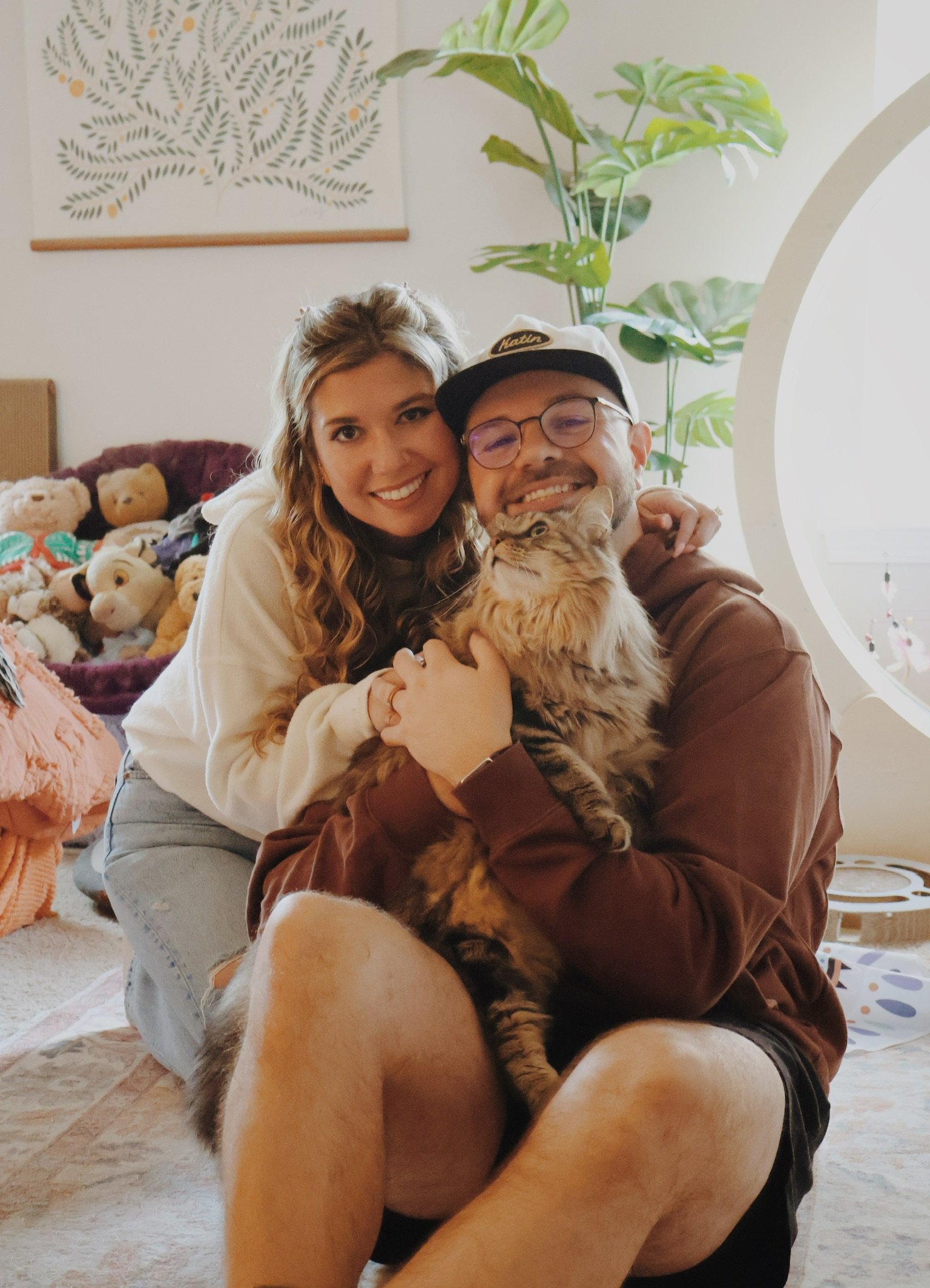 Nicole hugging Ian from behind as he holds a long-haired cat on his lap.
