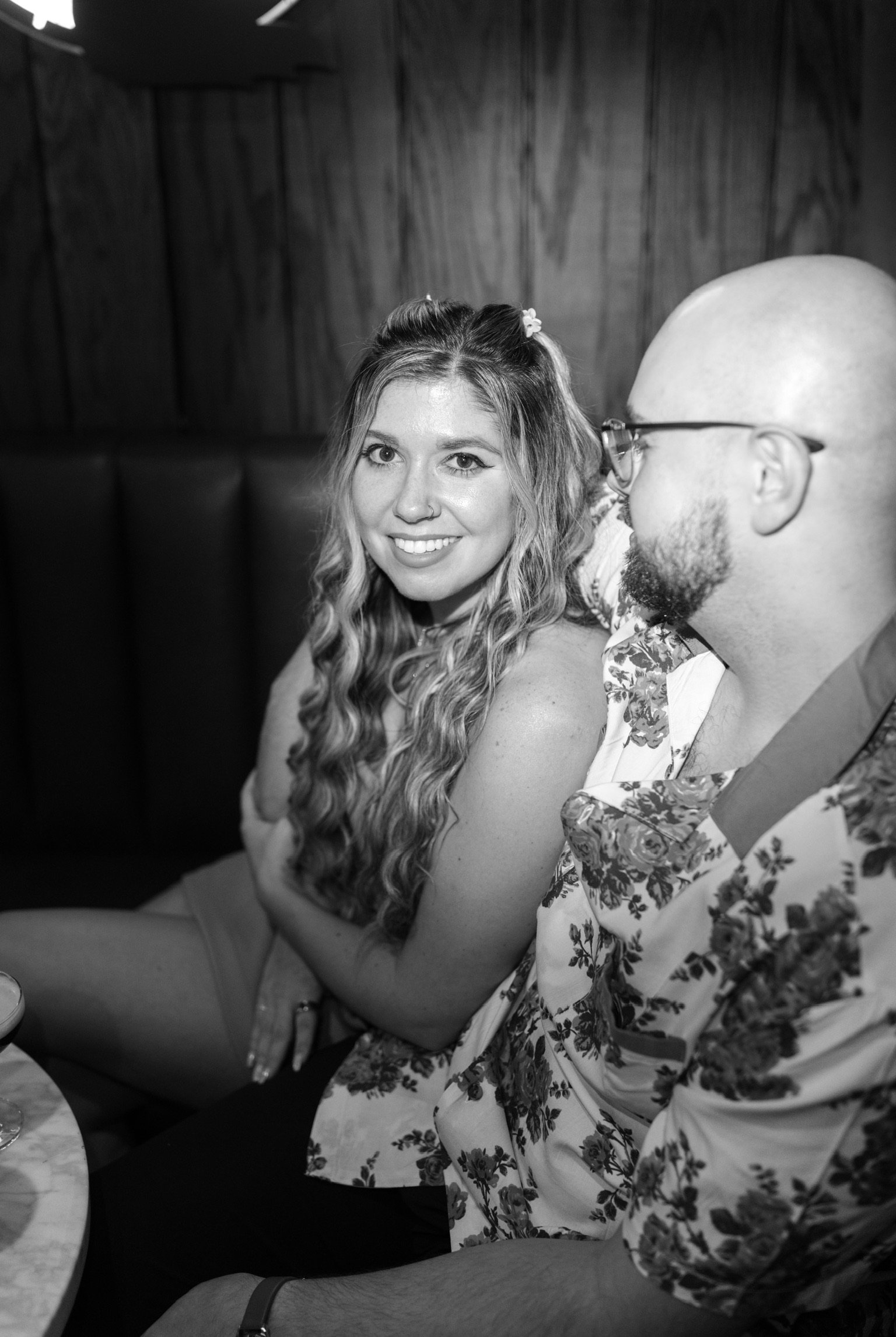 In black and white: Nicole smiling over her shoulder in a leather booth, Ian at her side.