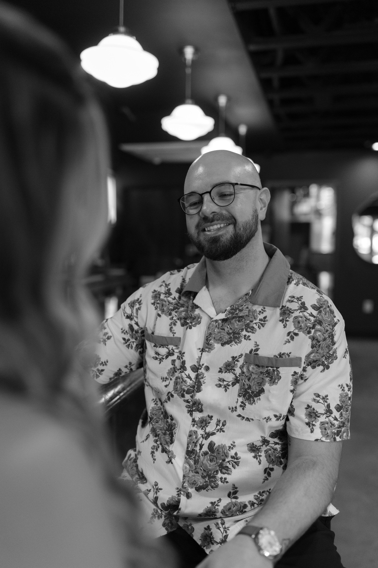 In black and white: Ian grinning across the bar at Nicole, the pendant lamps above him.