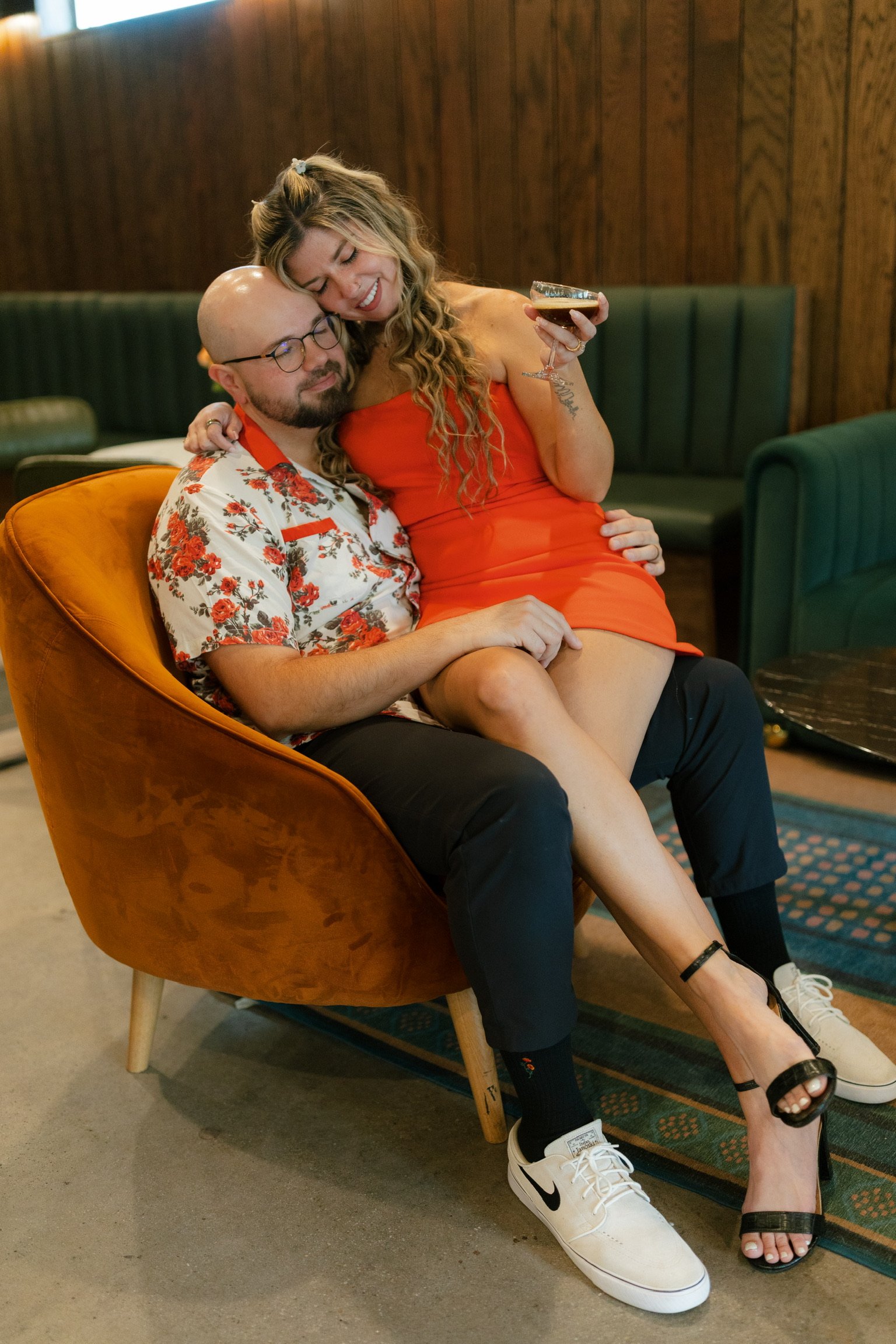 Nicole curled up in Ian’s lap in a mustard velvet armchair, laughing.