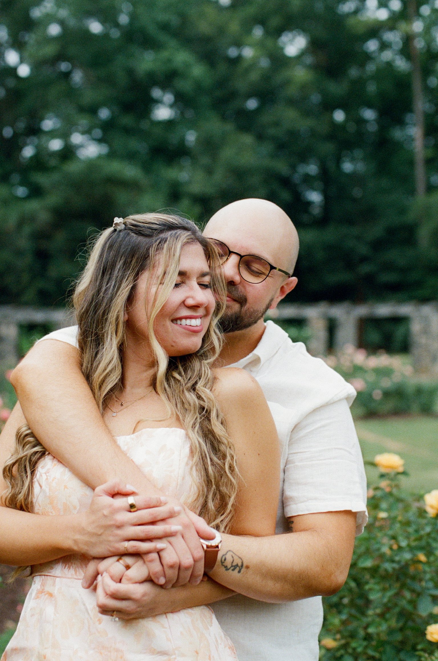 Ian hugging Nicole from behind among the roses, the two of them laughing.