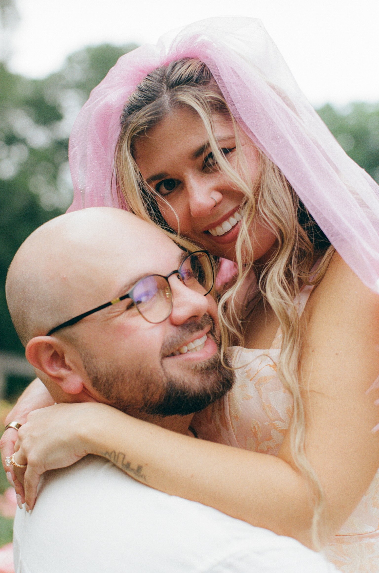 Close up: Nicole in her pink veil hugging Ian around the neck, both smiling.