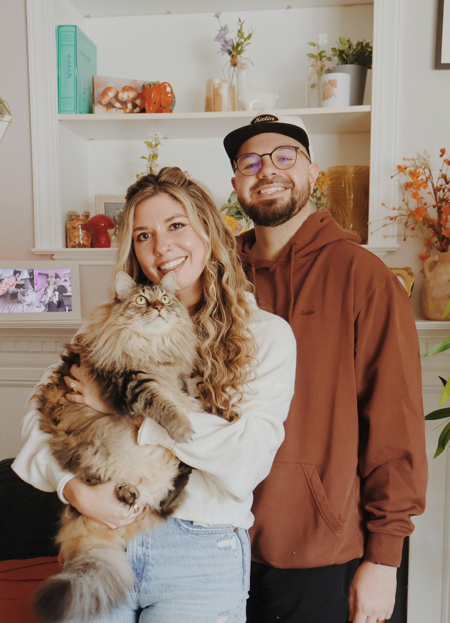 Nicole cradling a huge long-haired cat, Ian smiling at her shoulder.