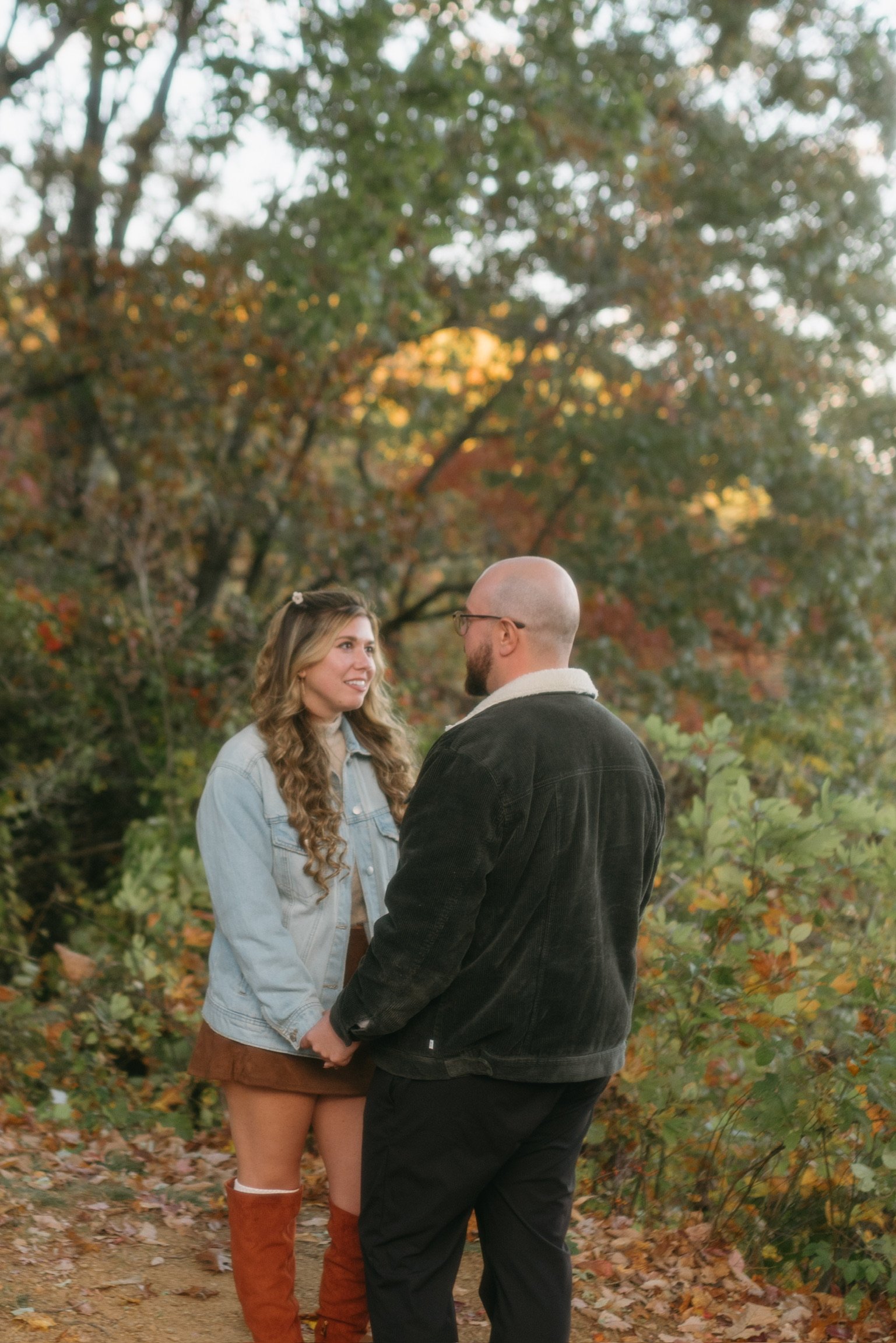 Nicole and Ian holding hands and facing each other among the autumn trees.