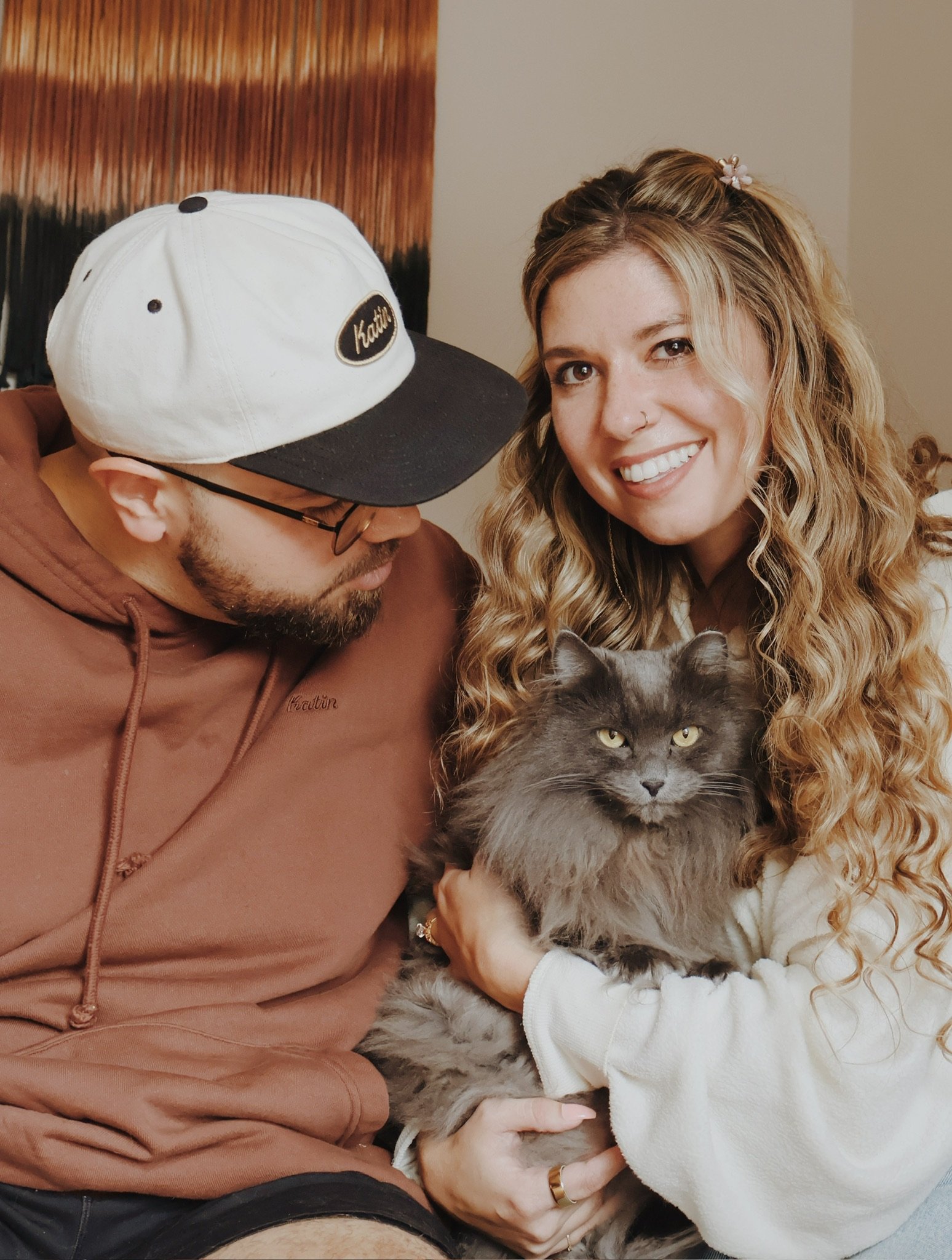 Nicole holding a gray long-haired cat, Ian leaning in beside her.