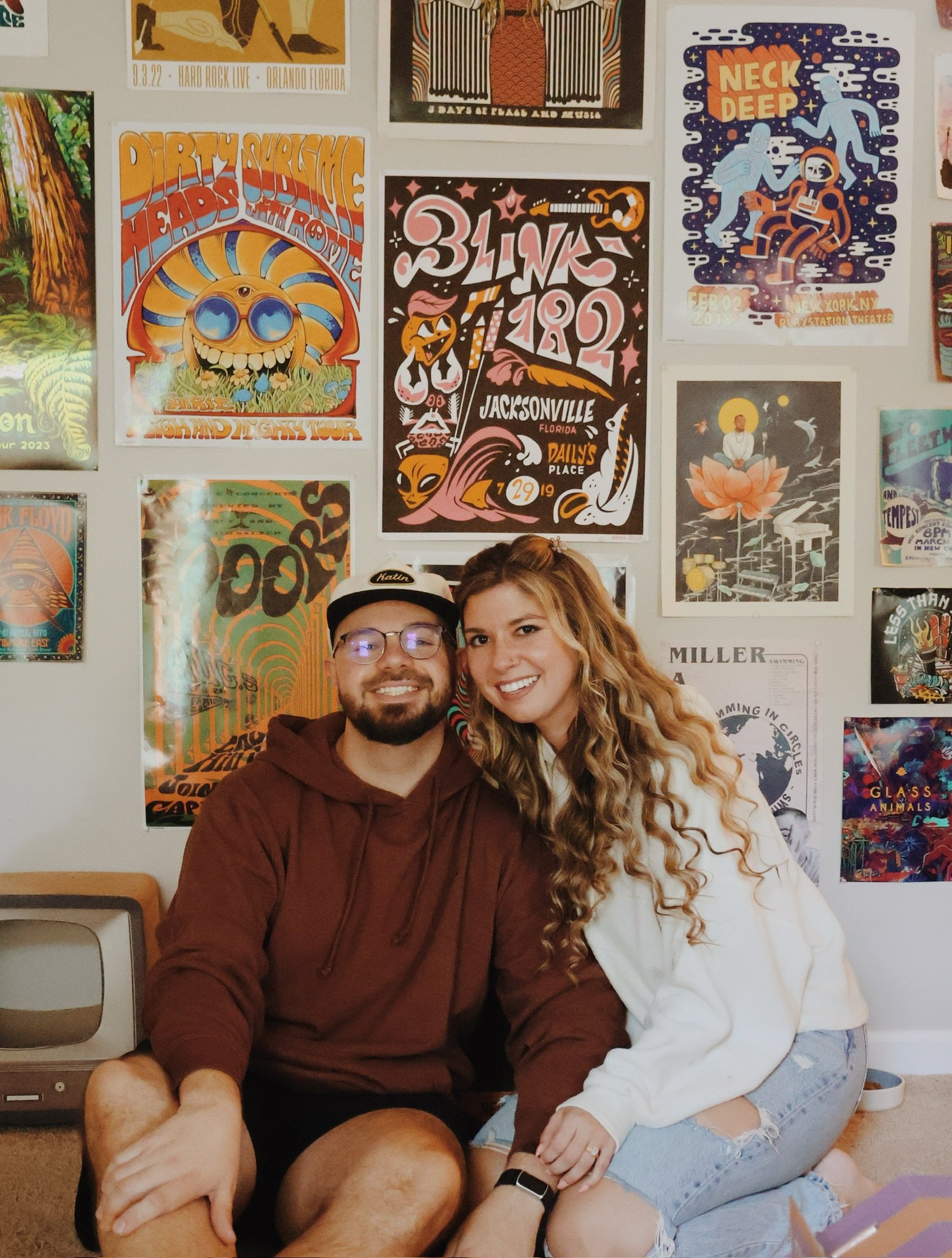 Nicole and Ian sitting against a wall covered in gig posters, her head on his shoulder.