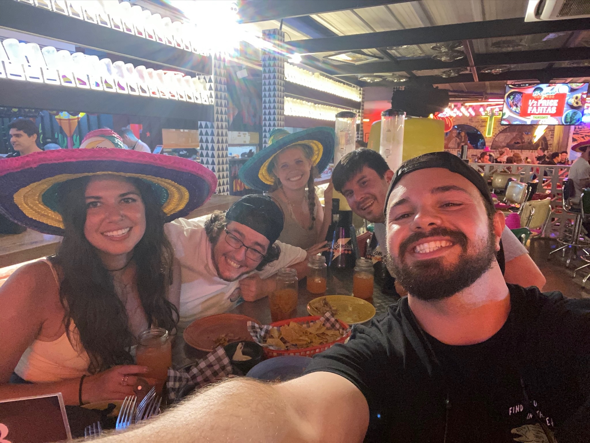 A selfie of friends at a bright, crowded Mexican restaurant, two of them in sombreros.