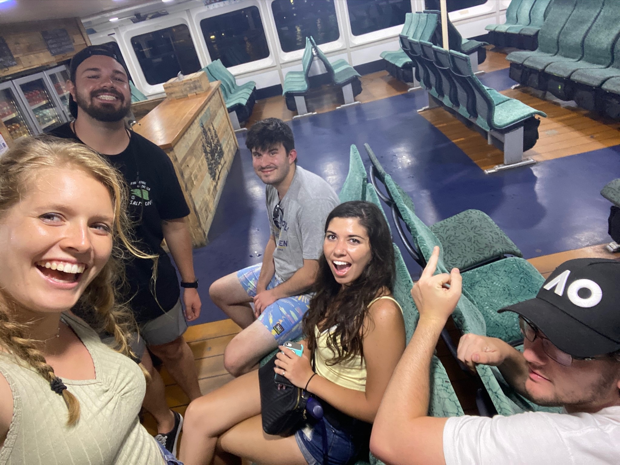 A selfie of friends grinning on board a ferry, one pointing straight at the camera.