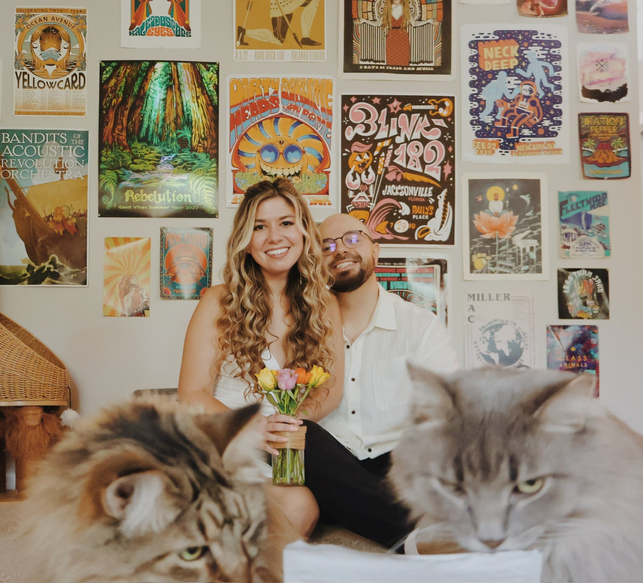 Nicole holding a jar of flowers with Ian at her shoulder, two big long-haired cats looming close to the camera.