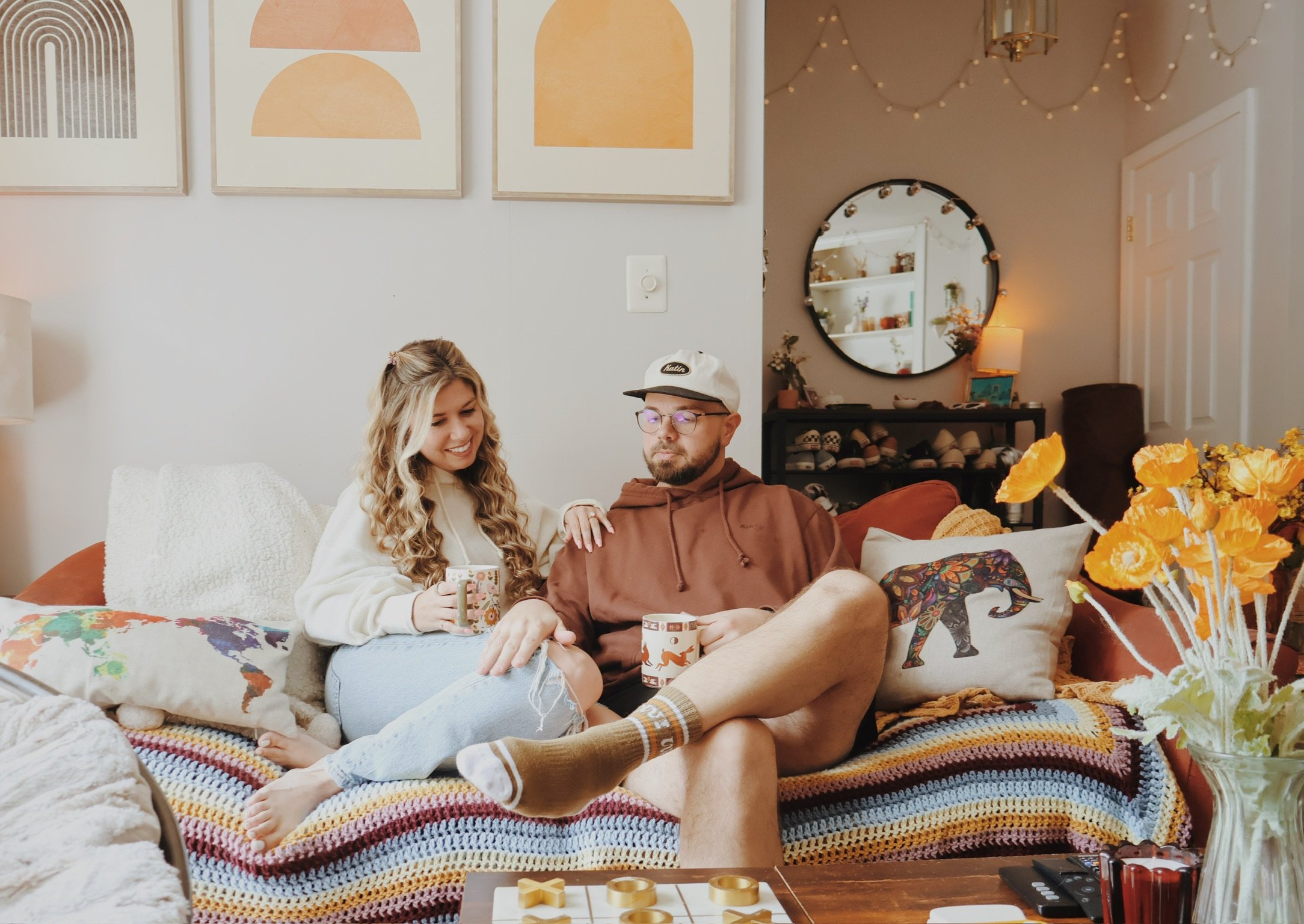 Nicole and Ian relaxing on a couch draped in a striped blanket, poppies and arched prints around them.