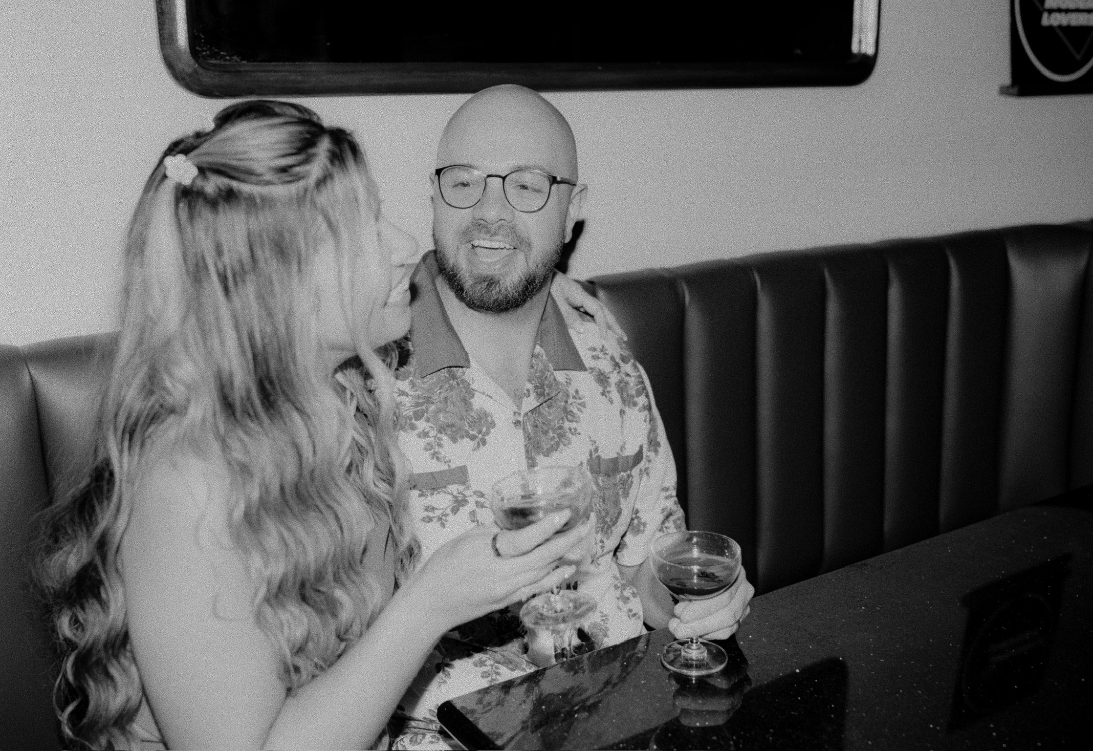 In black and white: Nicole and Ian in a leather booth, drinks on the table, Ian beaming.