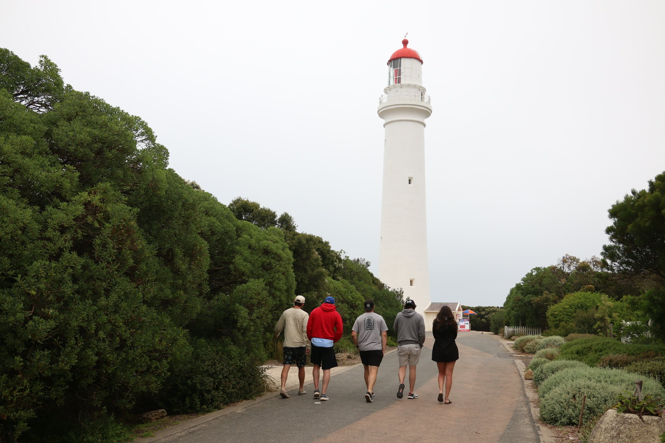Friends walking up the path toward a white lighthouse with a red cap.