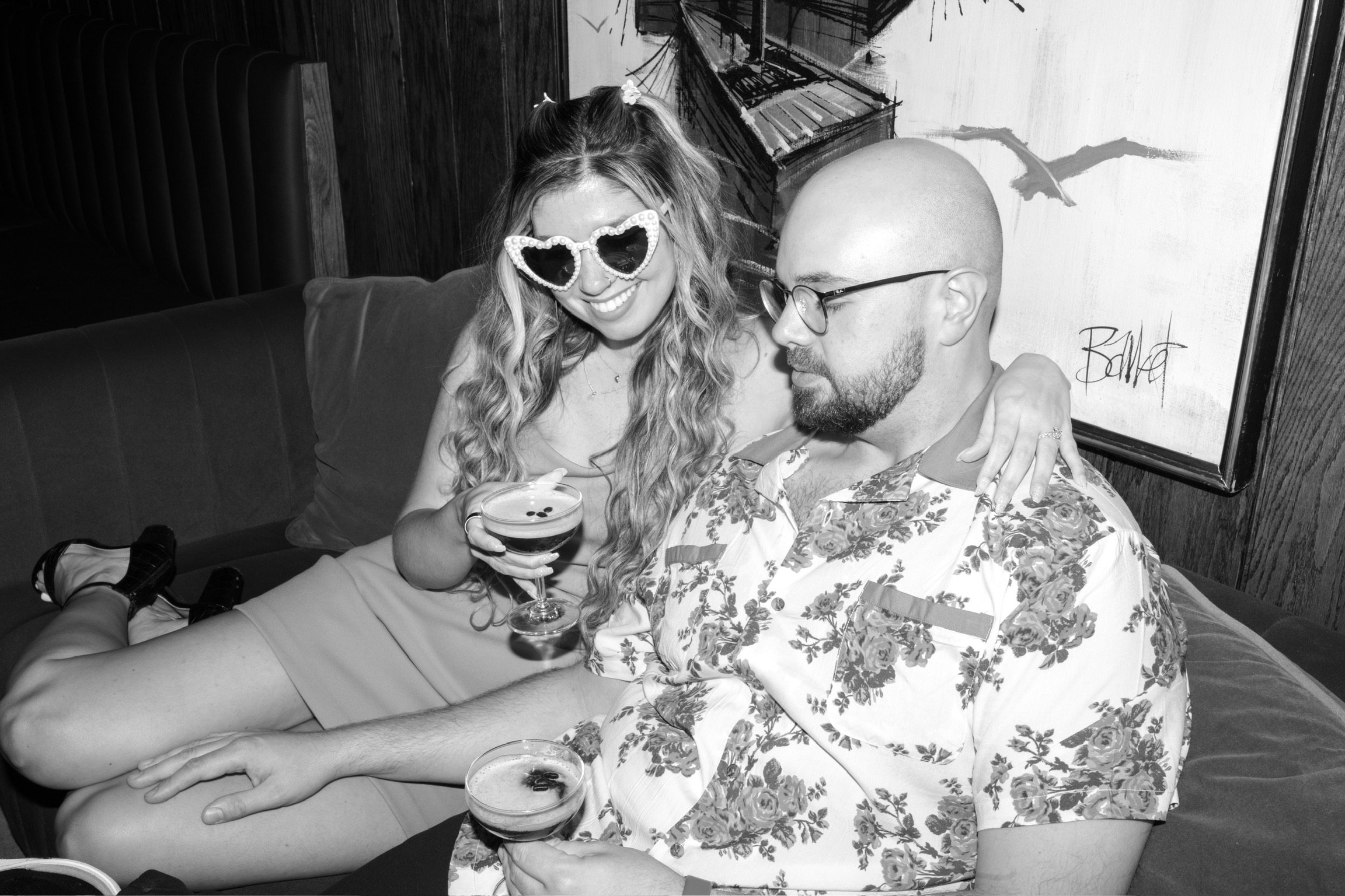 In black and white: Nicole in heart-shaped sunglasses on the banquette with Ian, cocktails in hand.